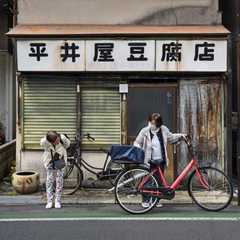 Two friends share a customary farewell, bowing outside an abandoned building in East Tokyo. 