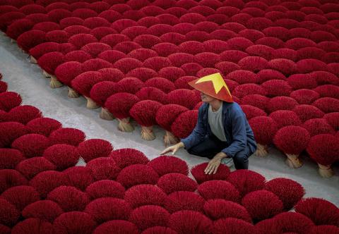 An asian worker tends to bundles of crimson incense