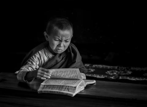 Young monk reading with a scowl on his face