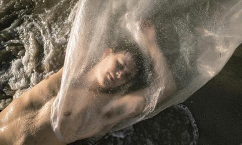 Man laying on the sand with a wet bag over the top of his body